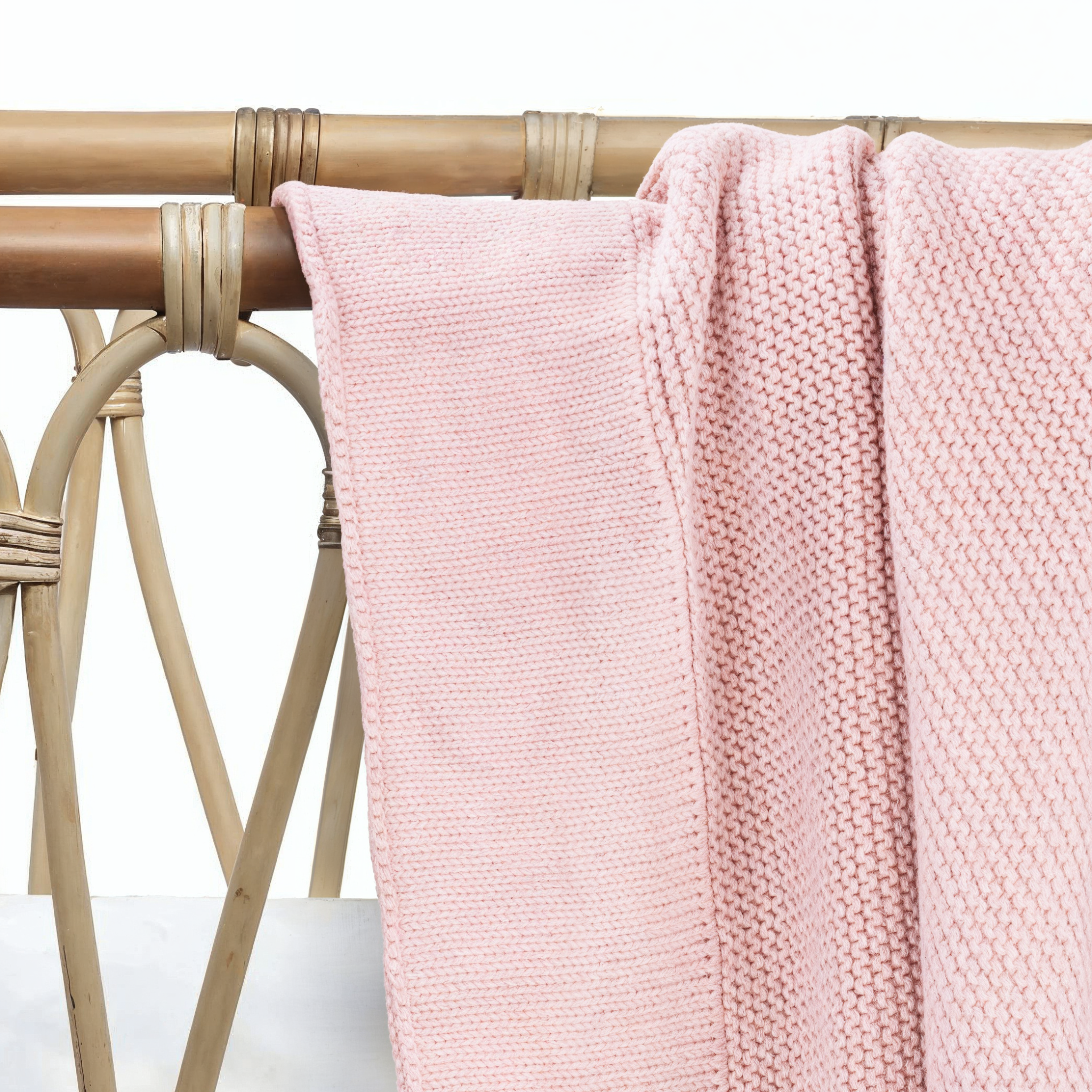 Soft pink cotton knit baby blanket draped over nursery furniture