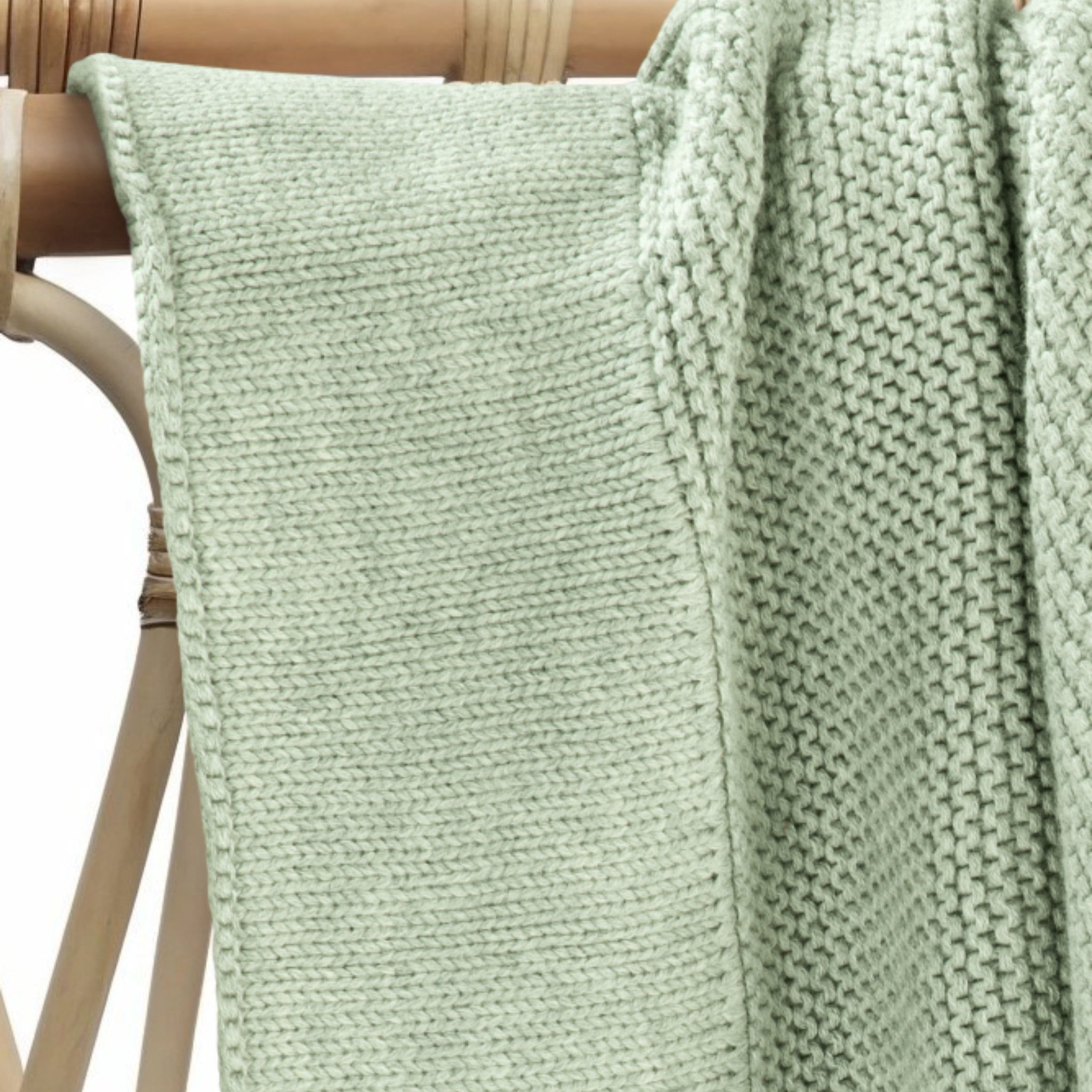 Soft cotton knit baby blanket in willow green draped gently over nursery furniture.
