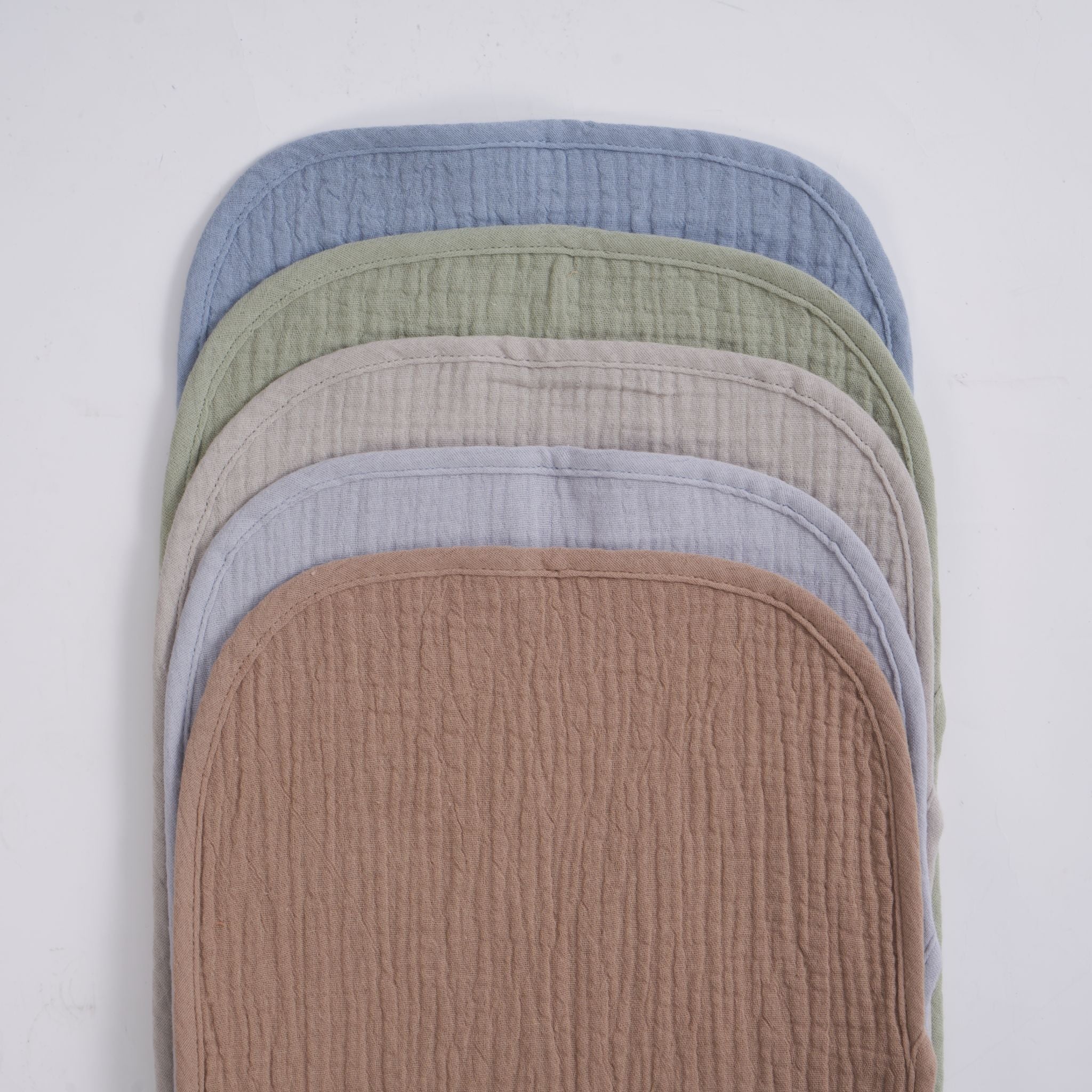 Organic muslin burp cloths in earth and sky tones draped over shoulder during feeding.