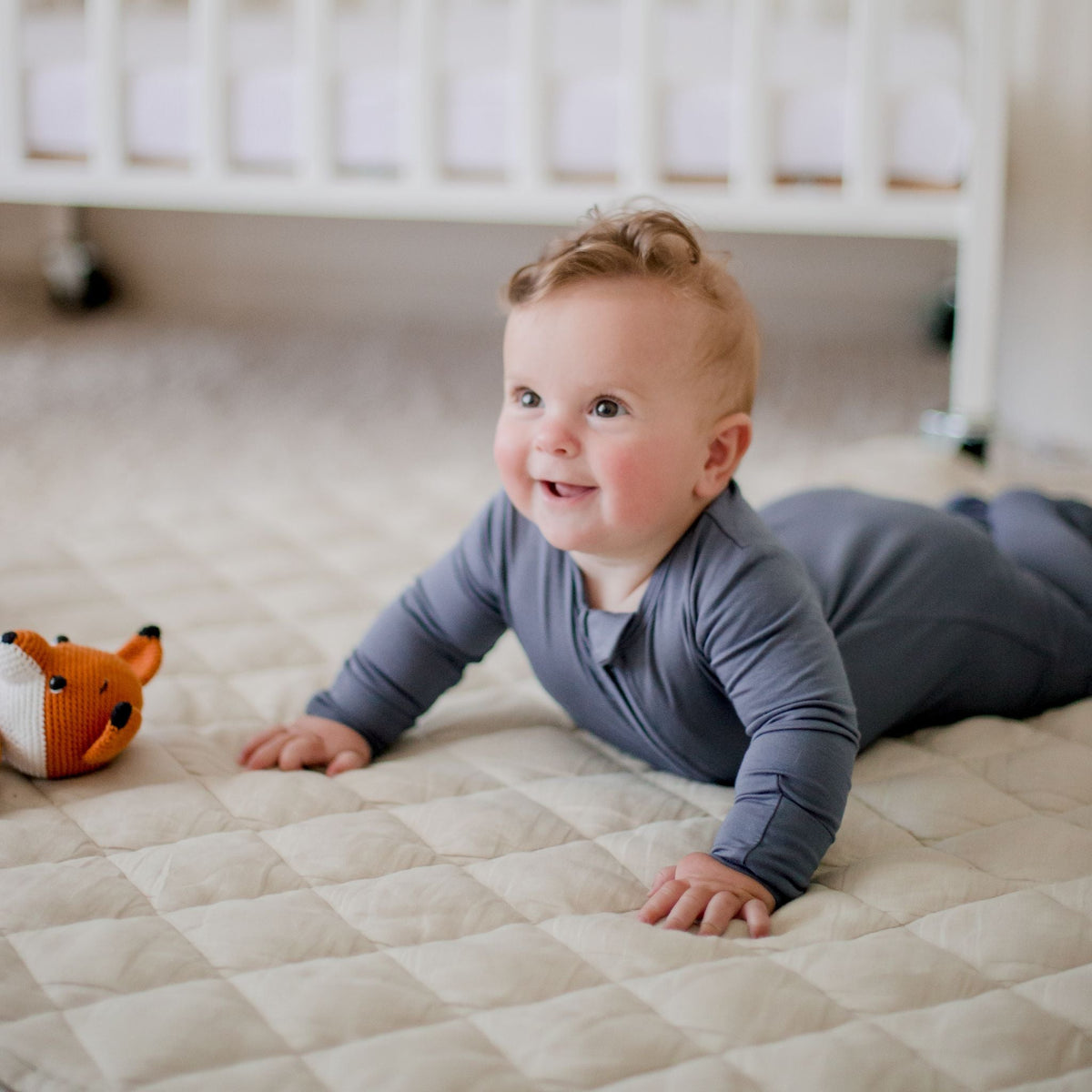 Smiling baby wearing a Zoe Sage bamboo zip romper during tummy time