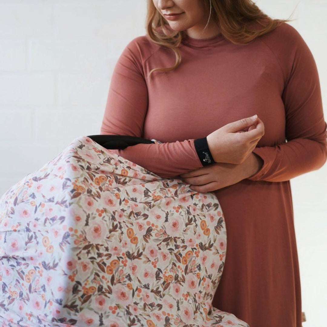 Mum in a rust top holding a floral 5-in-1 Mama Cover with a Nurselet bracelet on her wrist
